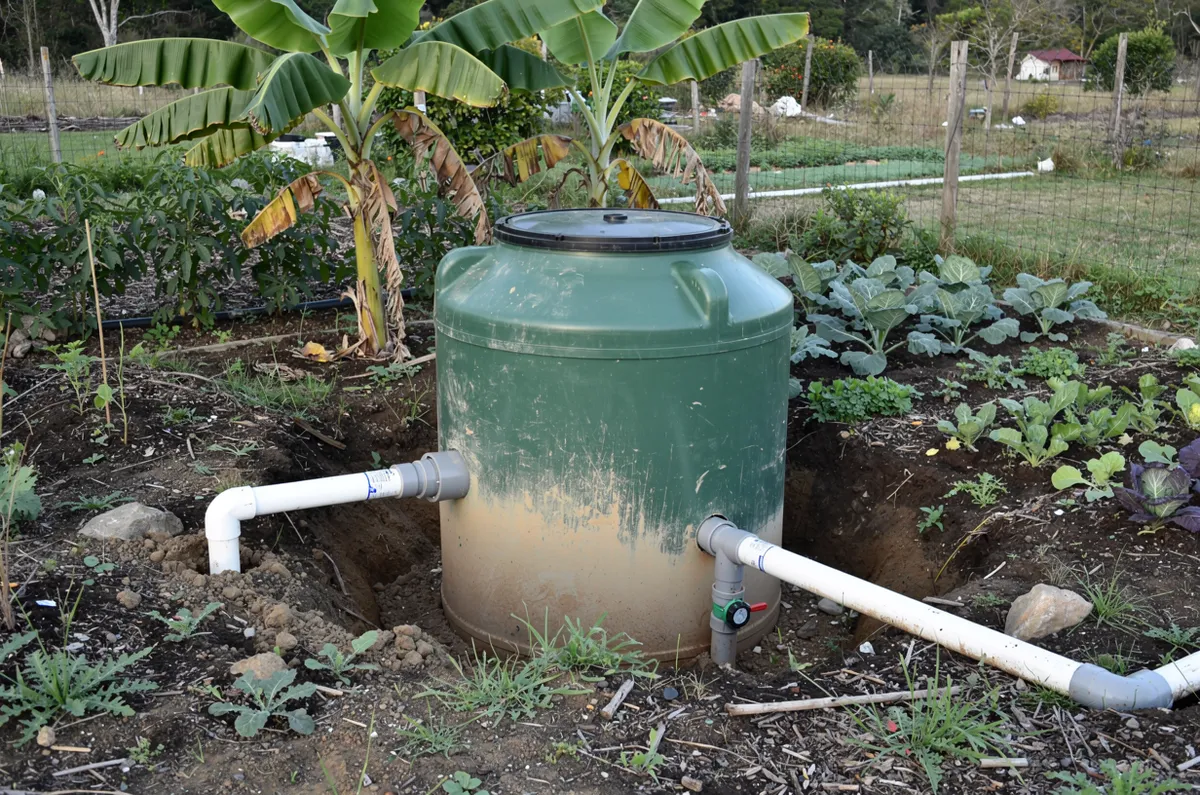 Fossa biodigestora verde instalada em horta com bananeiras, tubos e válvula